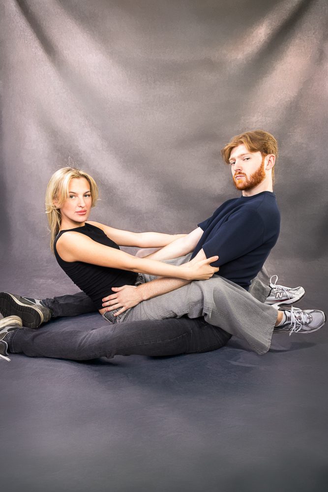 Couple tangled together on the studio floor in a deliberately awkward pose, deadpan expressions
