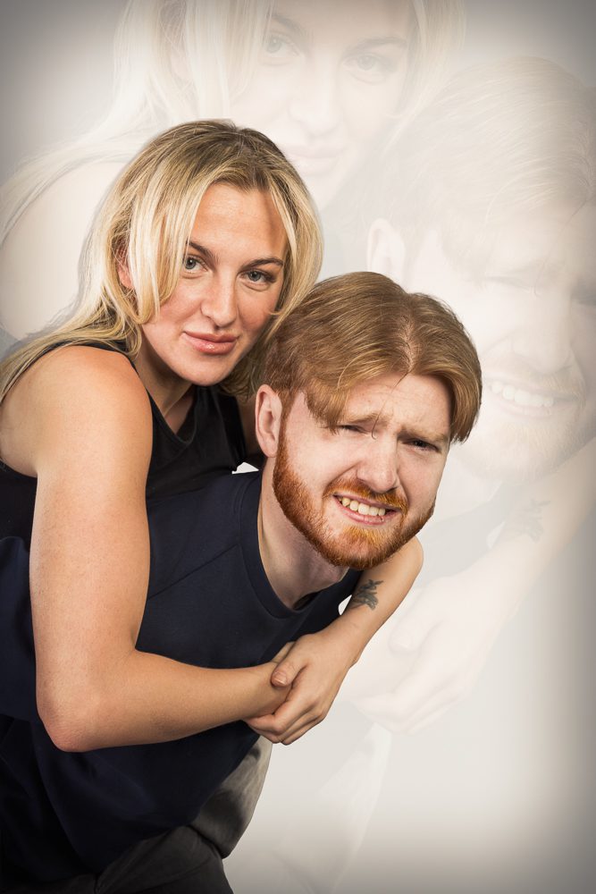 Couple in an exaggerated awkward studio portrait pose against a grey backdrop