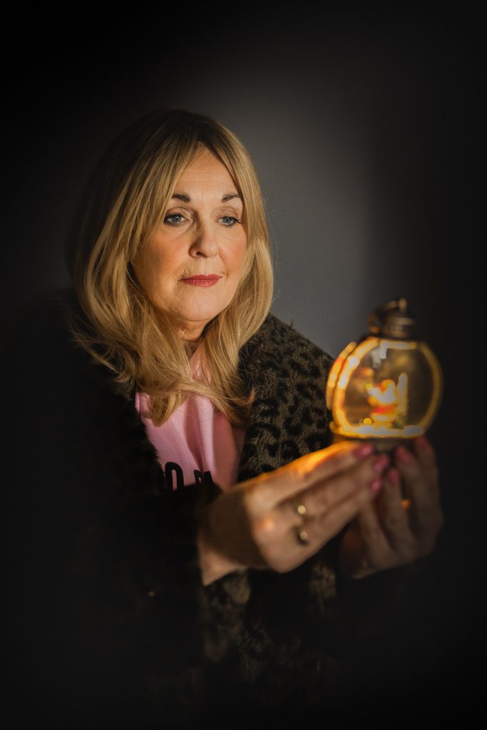 Cath Rice holding a lit snowglobe, promotional portrait for Slay Belles