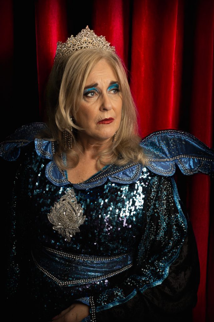 Cath Rice in character as the Wicked Queen against a red theatre curtain, Slay Belles