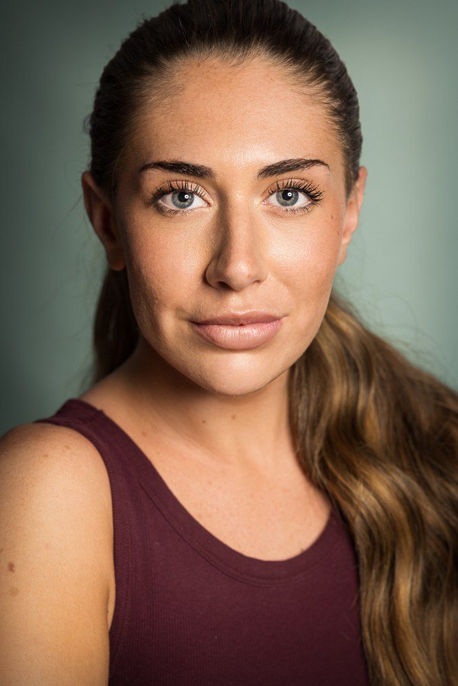 Summer headshot portrait, hair in ponytail, maroon top, sage green backdrop